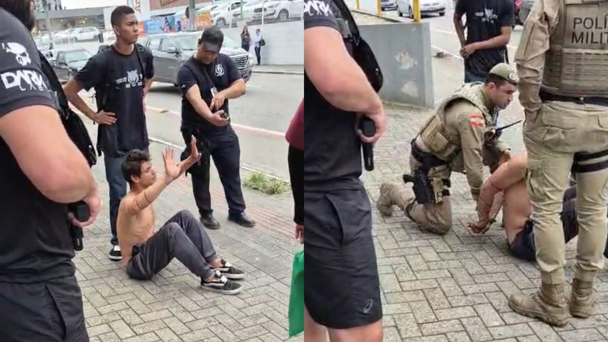 Suspeito sentado na calçada com as mãos erguidas, cercado por seguranças, em frente ao Terminal Urbano de Brusque